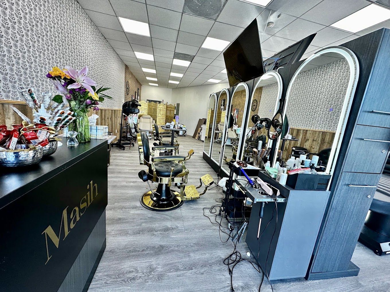Inside Masih Hair Salon & Barbershop, gold-framed arched mirrors, black leather barber chairs, and the reception desk with the Masih wordmark.